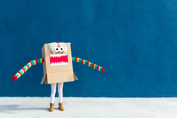Unrecognizable playful kid wearing funny costume of monster made of carton box standing on street during holiday celebration