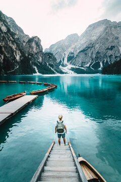 Back view of unrecognizable male traveler standing on wooden quay and admiring amazing scenery of lake with turquoise water in mountains on foggy day