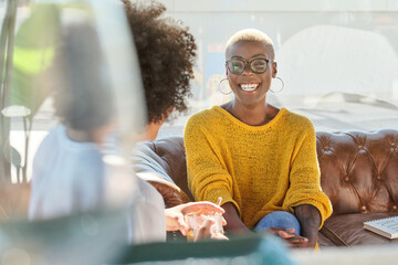 African American female with short hair speaking to unrecognizable friend with curly hair sitting on terrace and talking laughing at jokes and looking at each other while drinking hot beverage