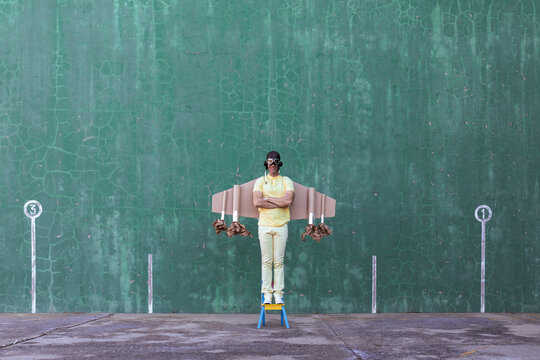 Cheerful male in handmade cardboard wings standing looking at camera while dreaming about achieving success