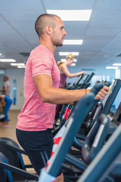 Side view of handsome male doing exercises on elliptical machine during cardio workout in modern sports club
