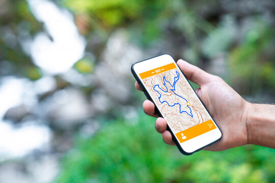 Cropped unrecognizable man traveler using smartphone browsing on map app standing on slope of amazing landscape of green forest with fast river