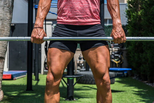 Crop of muscular male athlete lifting barbell and doing clean and jerk exercise during training on sunny day