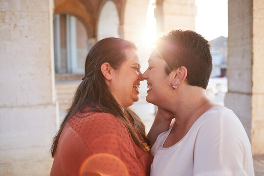 Side view of homosexual couple of women kissing with closed eyes near old house in sunlight in back lit