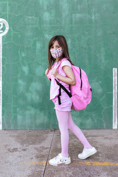 Side view of schoolgirl with rucksack and in protective mask standing on the street during coronavirus epidemic