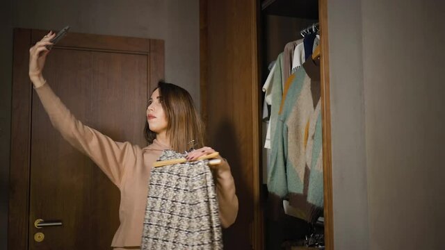 Young female fashion blogger live streaming wardrobe check or chosing clothes