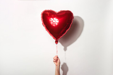 female hand holds a red air balloon in the form of a heart on a white background.