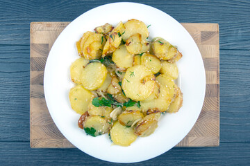 cooked fried potatoes with herbs and vegetables in a plate on a wooden table