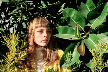 Portrait of a young blonde caucasian girl with blue eyes among the green plants of the park