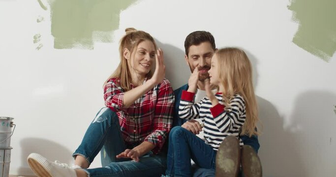 Happy family couple speaking with little cute preschool girl child choosing decor of new kid room during house renovation and home repair. Parents and pretty daughter chatting during remodeling room