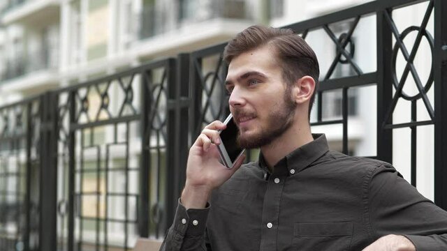 Slow Motion Young man sits on the bench and speaks on smartphone, he smiles and he is in a good mood