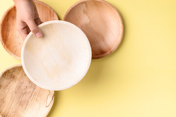 Hand holding betal palm leaf plate (Biodegradable, Compostable, Disposable or Eco friendly plate) on yellow background, Sustainable concept