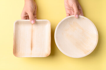 Hand holding betal palm leaf plate (Biodegradable, Compostable, Disposable or Eco friendly plate) on yellow background, Sustainable concept