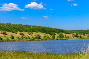 Summer landscape with beautiful lake, green meadows, hills, trees and blue sky