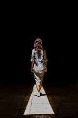 A woman in a skirt walks along a beam of light in the dark