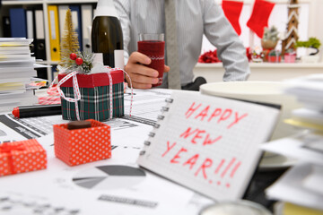 Naklejka na ściany i meble Business and holiday concept - businessman celebrating in office decorated with Christmas tree, candies and other new year decoration. Shows a notepad with happy new year text