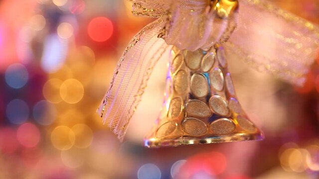 A beautiful Christmas tree toy hangs against the background of colorful garlands and moves slightly. Close-up. Christmas tree toy in the form of a golden bell
