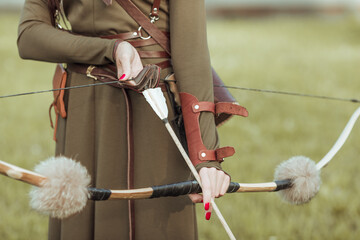 Young woman warrior with a bow pulls the bowstring with an arrow, close-up
