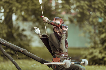 Woman with arrows and a bow sits on a fallen tree and puts an arrow in a quiver