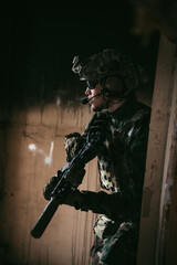 Military man with assault rifle standing inside building, he is ready for combat
