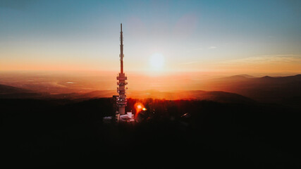 Silhouette of high Kekes Television Tower standing on hungarian Kekes Mountain during epic golden sunset in background. Beautiful scenic lighting landscape, Hungary. Aerial flight.