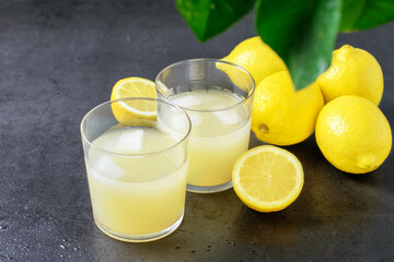 Glasses of lemon juice and fresh ripe lemon fruits on the gray background. Healthy dietary eating...