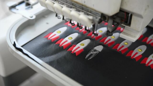 Close up view of working sewing machine that making rocket pictures on black cloth.