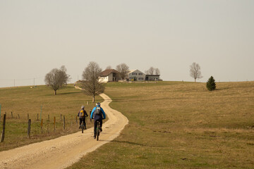 Obraz premium Two mountain bikers on a gravel road in front of a farm in the Swiss Jura hills