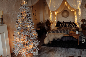 Photo of cozy decorated bedroom. Big canopy bed with soft blanket and light garland, near fireplace and Christmas tree. Winter holidays, xmas background, interior design concept