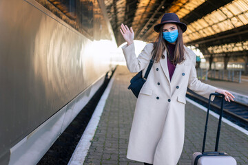 Fototapeta na wymiar Positive female tourist in mask waiting for the train at the railway station. Woman in medical mask at an empty train station