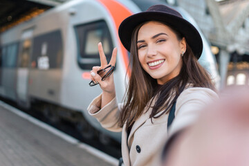 Girl tourist takes selfie at the railway station against the background of the locomotive. Girl talking on video call