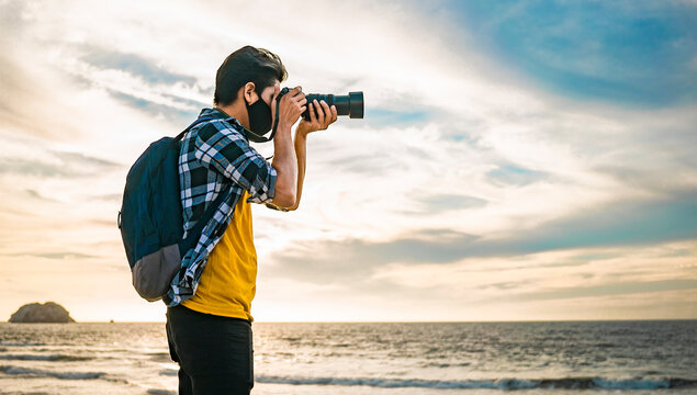 chico latino  fotografiando el mar con c&aacute;mara en mano y cubrebocas