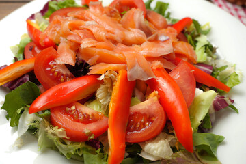 Serving of fresh salad with tomato, sweet pepper, lettuce and smoked salmon on a white plate. Healthy eating option.