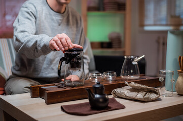 Fototapeta na wymiar A young man is studying the art of traditional chinese tea ceremony. Brews ripe raw tea in a special glass bowl on a bamboo tray