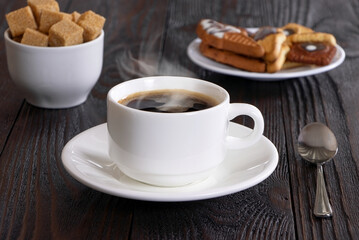 A cup of coffee and cake on a wooden background. Morning hot coffee and pastry on a wooden table. A white coffee cup and cane sugar. Steam.Espresso.