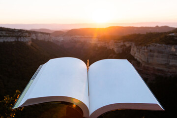 Open book with blank pages with a beautiful sunset or sunrise landscape in the background. Concept of going out into nature to disconnect as a source of inspiration, education and wisdom.