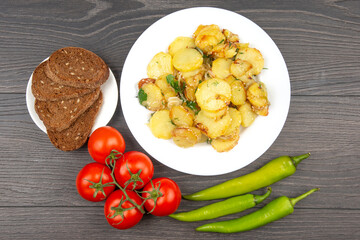 cooked fried potatoes with herbs and vegetables in a white plate on a wooden table