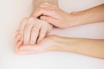 Young woman's hands hold grandmother's hands, an elderly patient. Handshake, caring, trust and support. Medicine, family and healthcare.