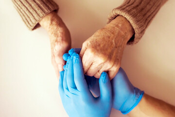 A doctor's hands in a blue gloves holds the hands of an elderly woman, a patient. Handshake, caring, trust and support. Medicine and healthcare.