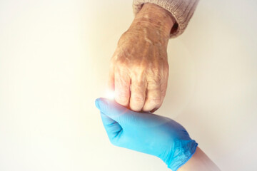 Handshake, caring, trust, treatment and support. The doctor's hand in a blue glove holds the hand of an elderly woman, he passes the light to the patient. Medicine and healthcare.