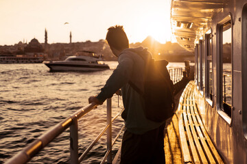 A young travelling man on a ferry floats to the shores of Istanbul, Turkey in the rays of sunset....