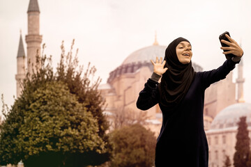 A young smiling Muslim girl in a hijab makes a selfie against the background of the Hagia Sophia mosque. Tourism in Istanbul, Turkey