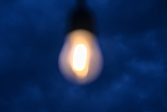 bokeh effect on calid lightbulb glowing over dark blue night sky