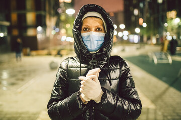 White medical gloves dress on hands adult woman on street city europe during the lockdown quarantine covid19, protective mask face, cityview evening.Personal health protection coronavirus infection