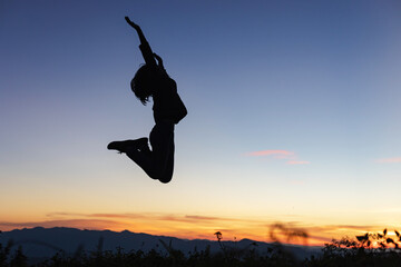 Silhouette of happy girl jumping playing on mountain at sunset