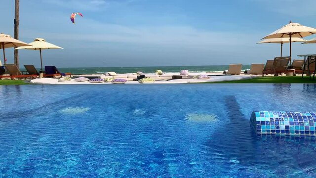 Swimming pool with the ocean beach and a person kite surfing or kiteboarding in the wind beyond the pool
