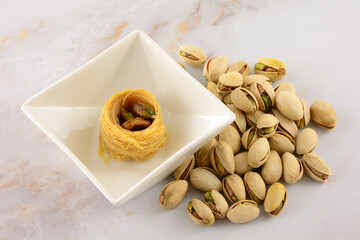 Piece of baklava bird's nest dessert with pistachio nuts inside placed in snack bowl with pistachio nuts