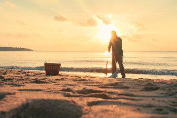 Fototapeta na wymiar Asian man cleaning sandy beach at sunrise