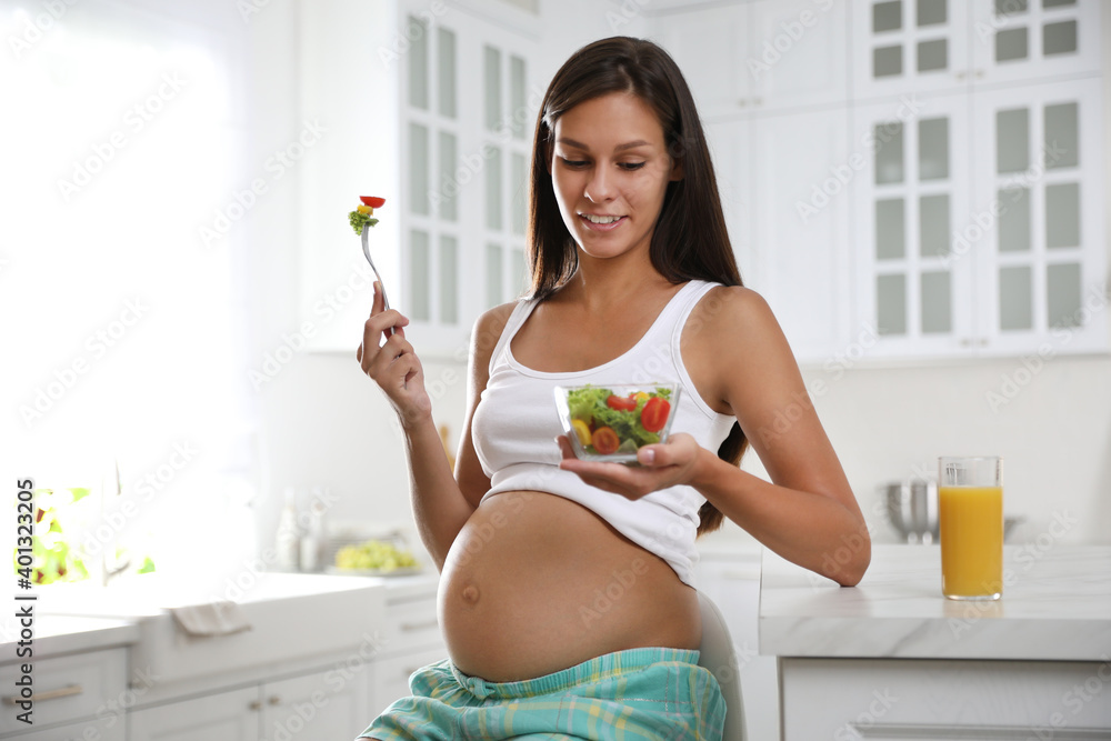 Canvas Prints Young pregnant woman with bowl of vegetable salad at table in kitchen. Taking care of baby health