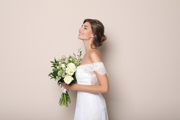 Young bride wearing wedding dress with beautiful bouquet on beige background